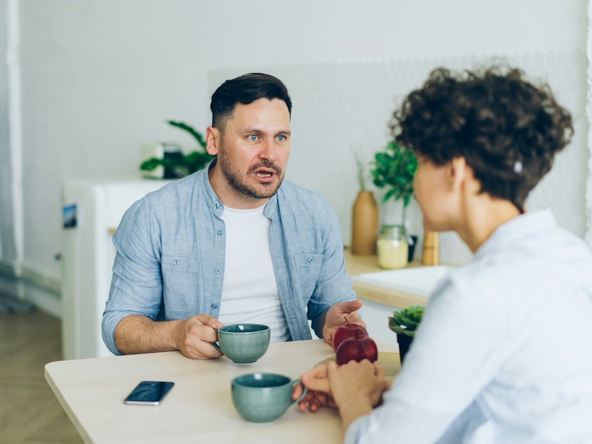Two people talk across a small table over cups of coffee