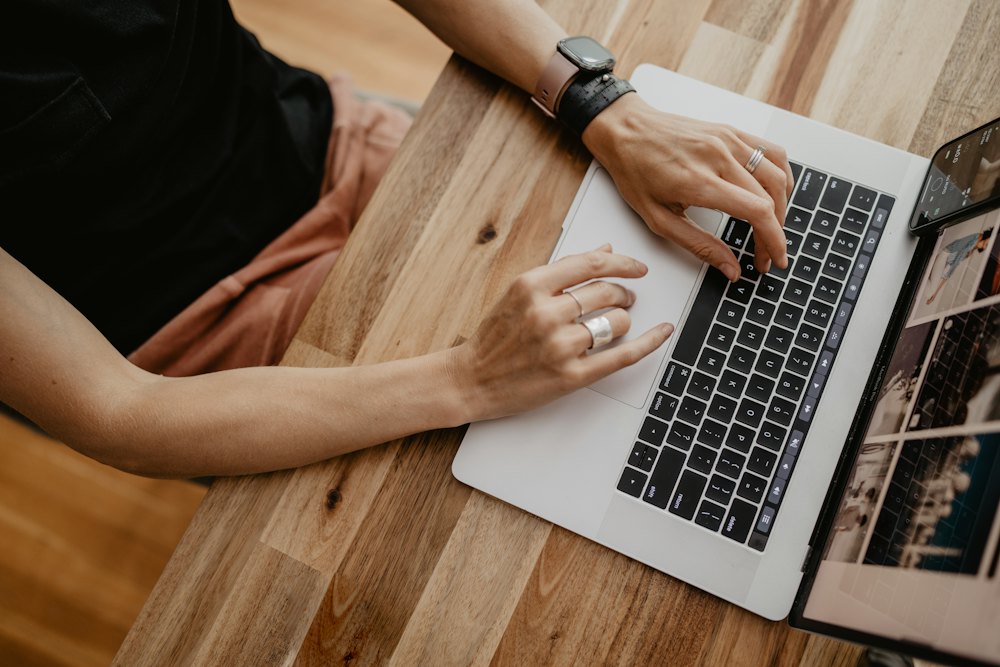 Hands typing on a laptop at a wooden desk, a grid of photographs on the screen.