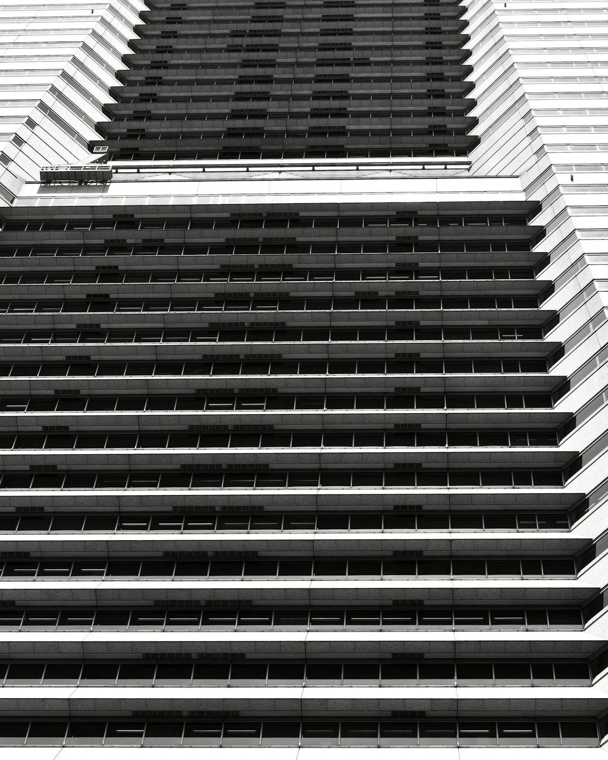 A black-and-white building facade of identical stacked balconies, seen from below.