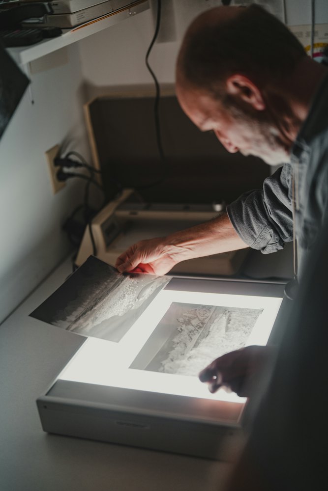 A reviewer leaning over a light table, checking a print by hand