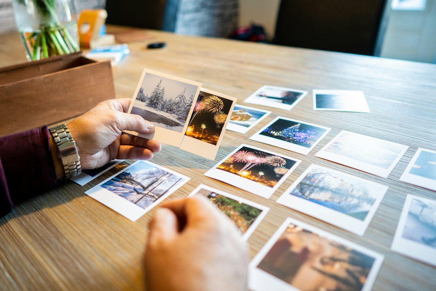 Hands sorting printed photographs across a wooden table