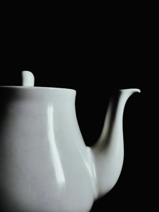A white porcelain teapot lit from the side against black
