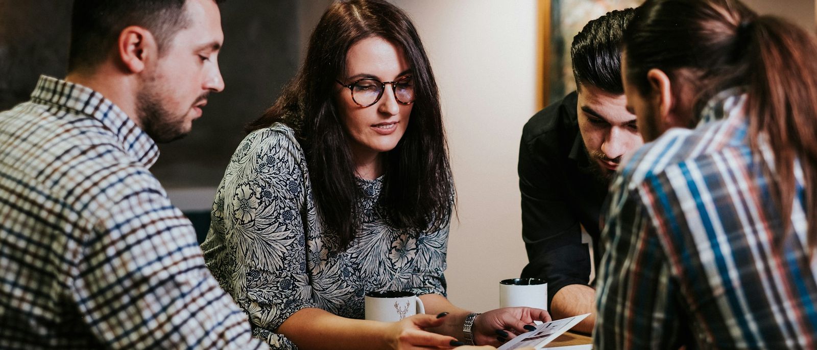 Four colleagues lean over printed pages at a table, reading a draft together