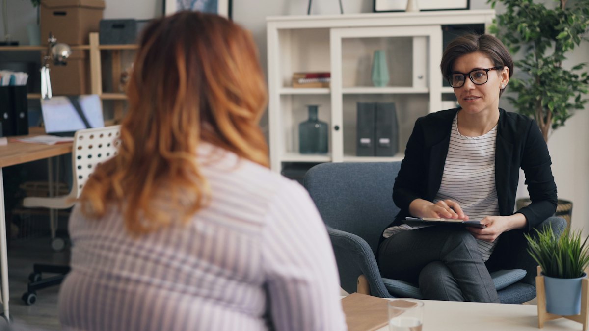 An interviewer with a notepad listens to a seated participant