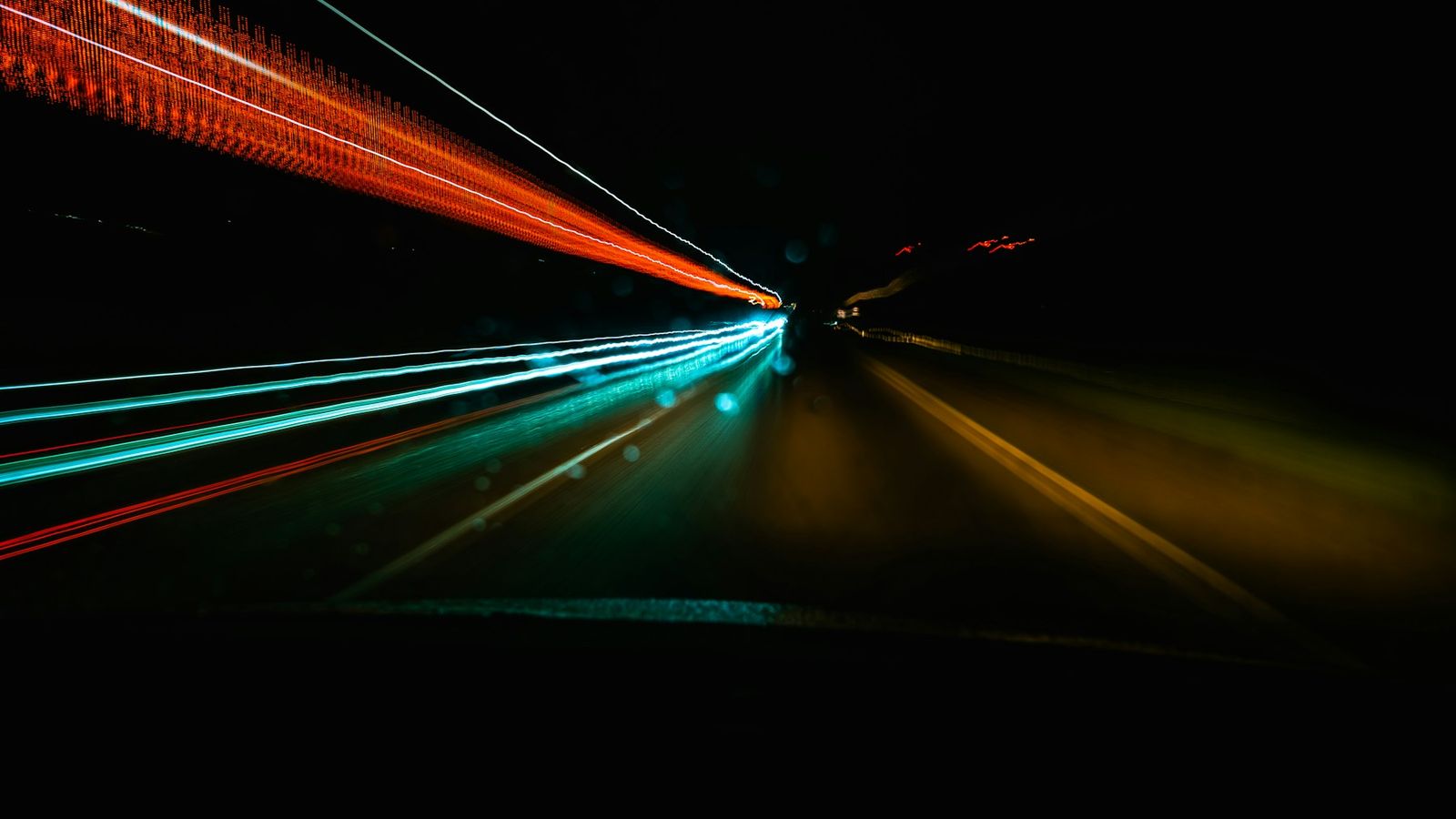 Long-exposure light trails streak along a dark road at night