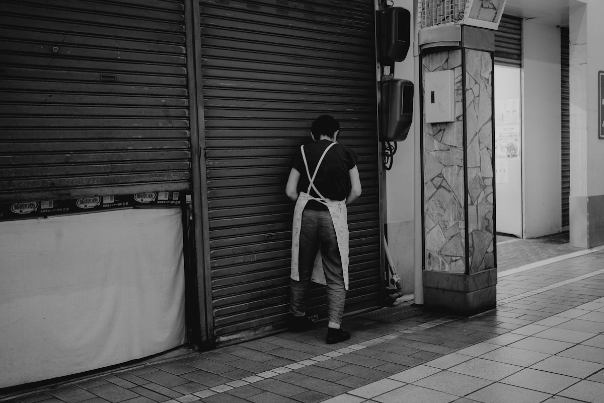 A person in an apron beside a closed metal shutter, in black and white, with the “Your brand” identity applied