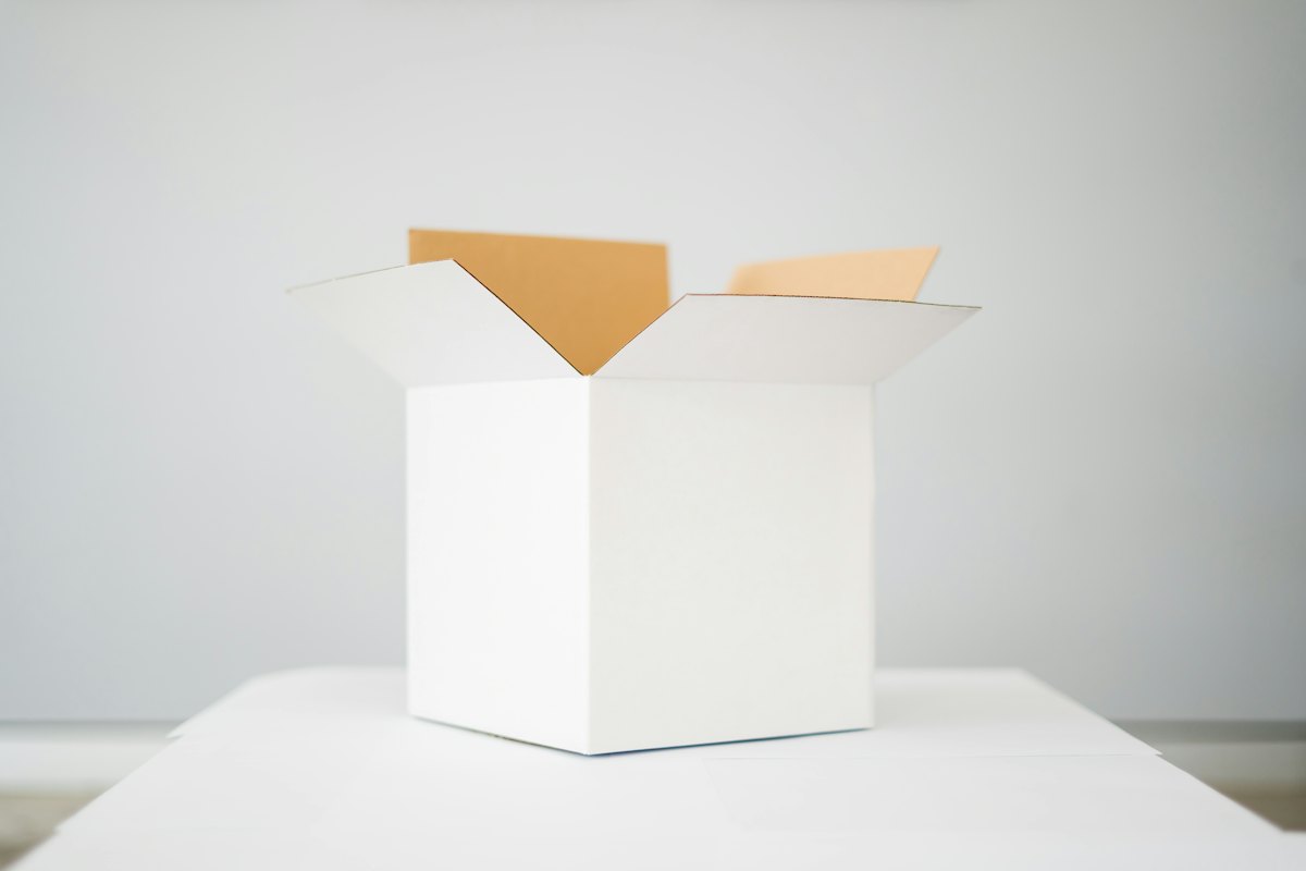 A plain white shipping box with open flaps on a white table, with the “Your brand” identity applied