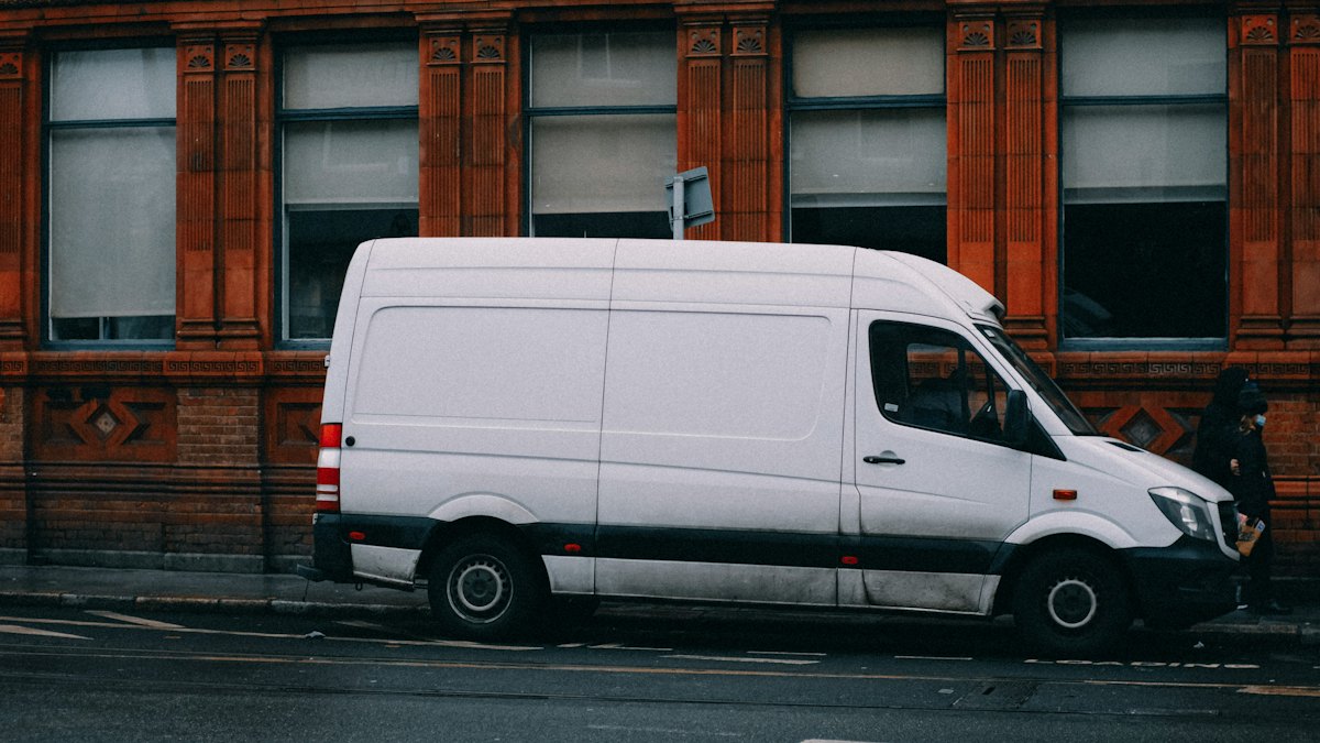 A plain white van parked on a city street, with the “Your brand” identity applied