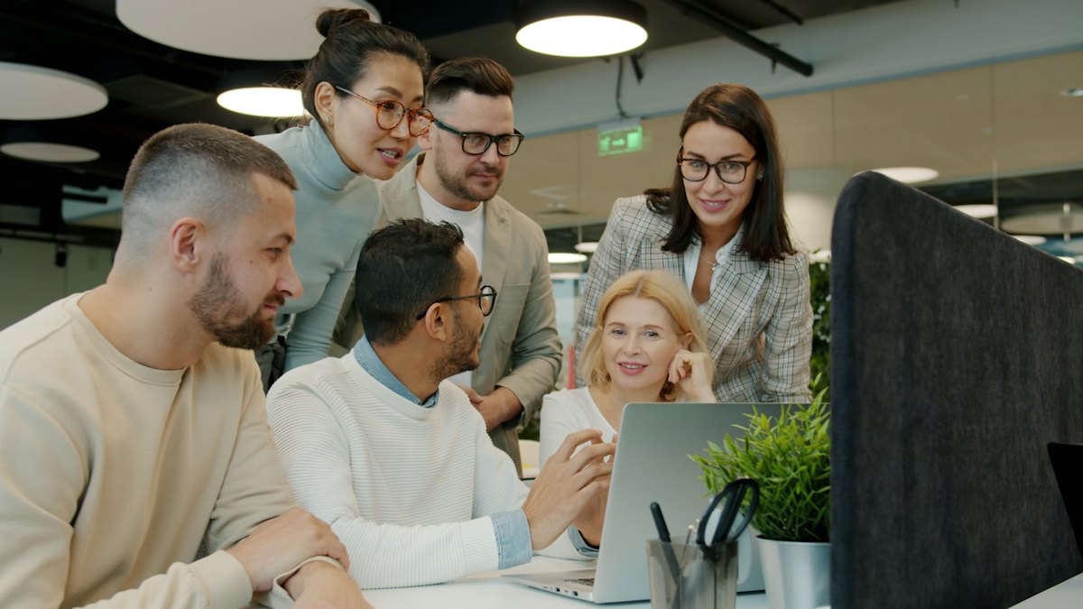 A team gathered around a laptop in an open office, talking through what is on screen