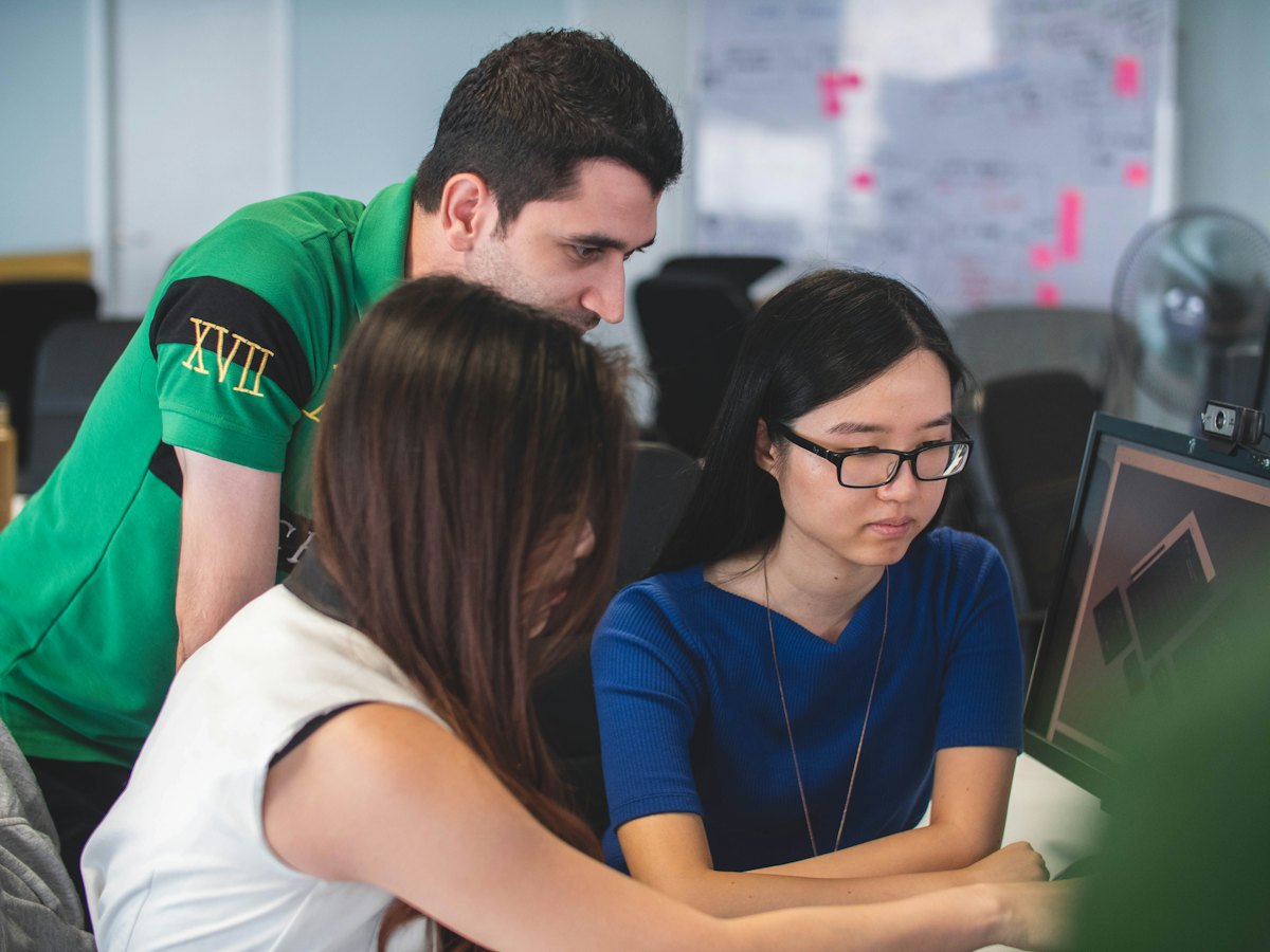 A small team gathered around a monitor, one person pointing at the screen