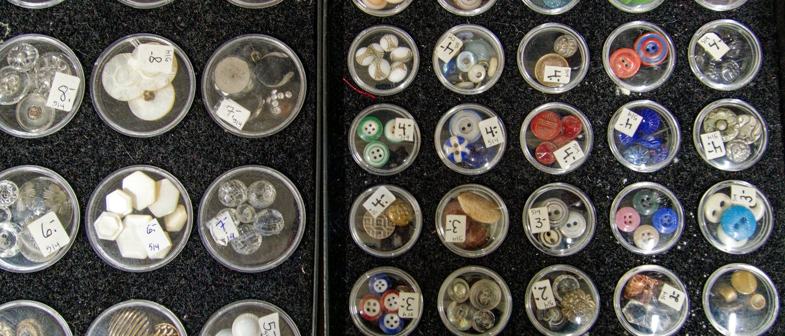 Trays of clear pots, each holding one kind of button, sorted and labelled by hand