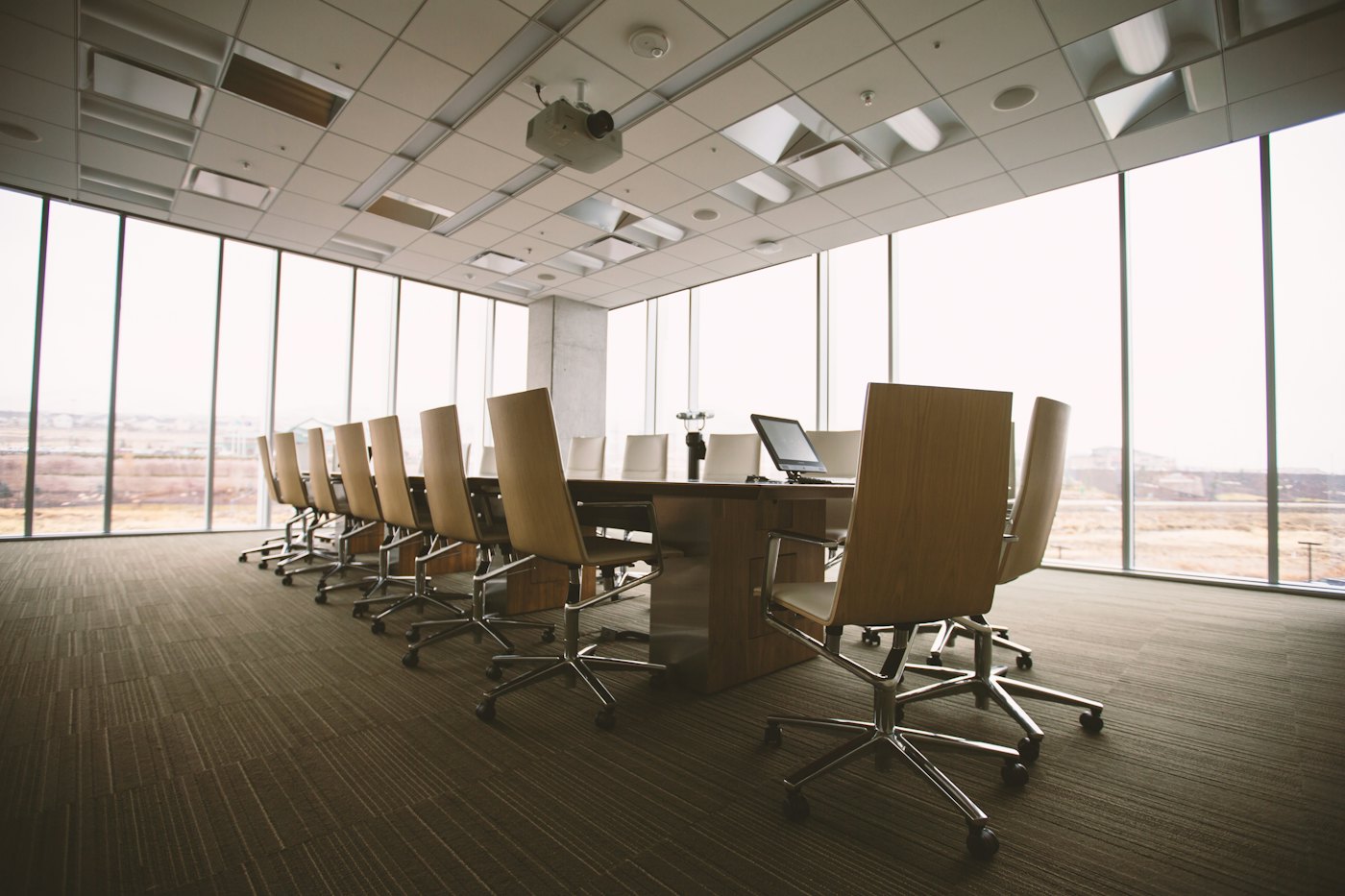 An empty boardroom with a long table and chairs facing floor-to-ceiling windows