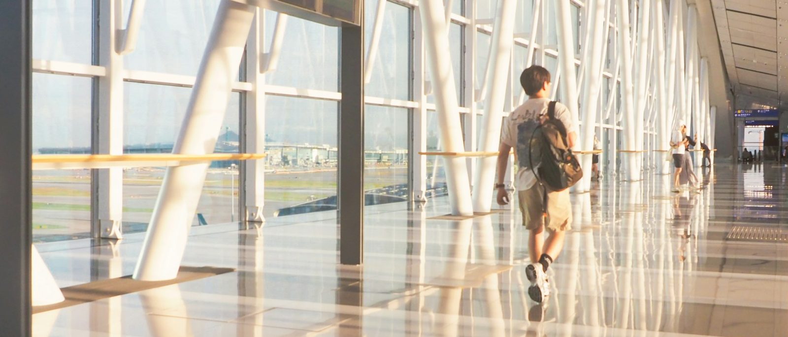 A traveller with a backpack walks through a sunlit airport concourse