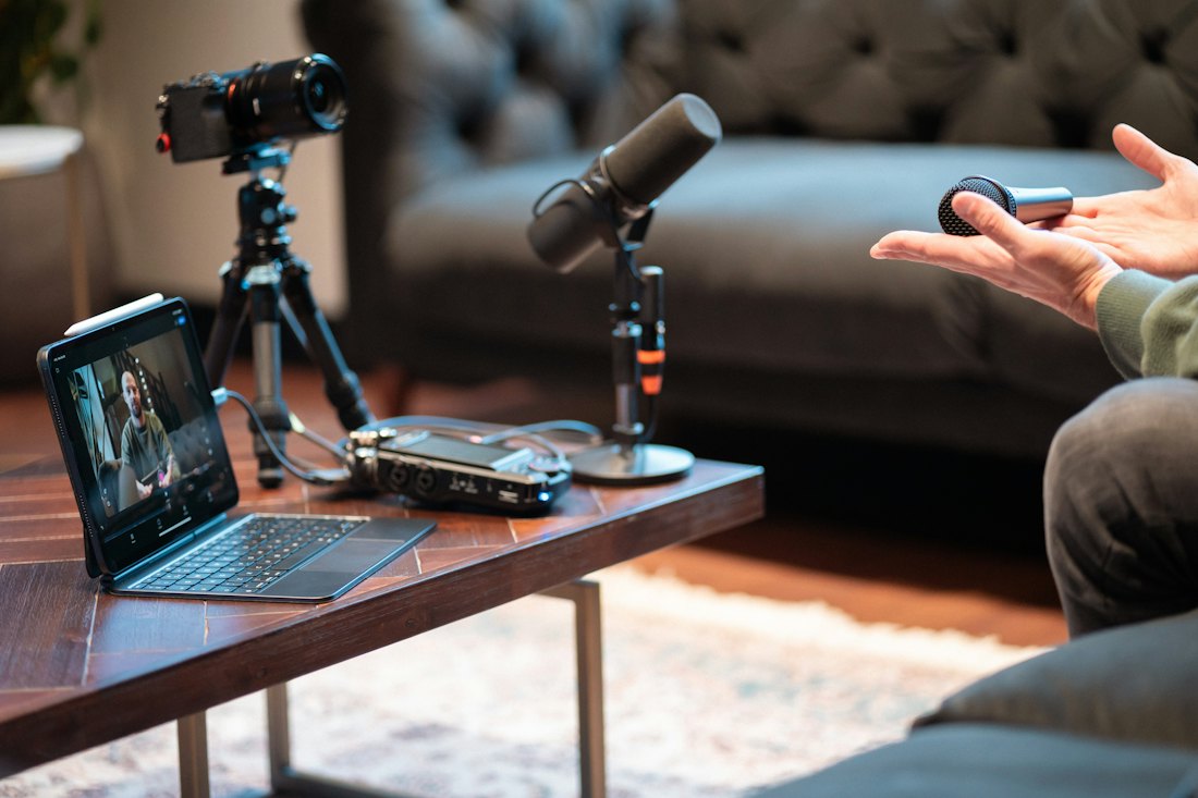 A camera on a tripod, a microphone and a tablet set up on a coffee table for a recorded interview