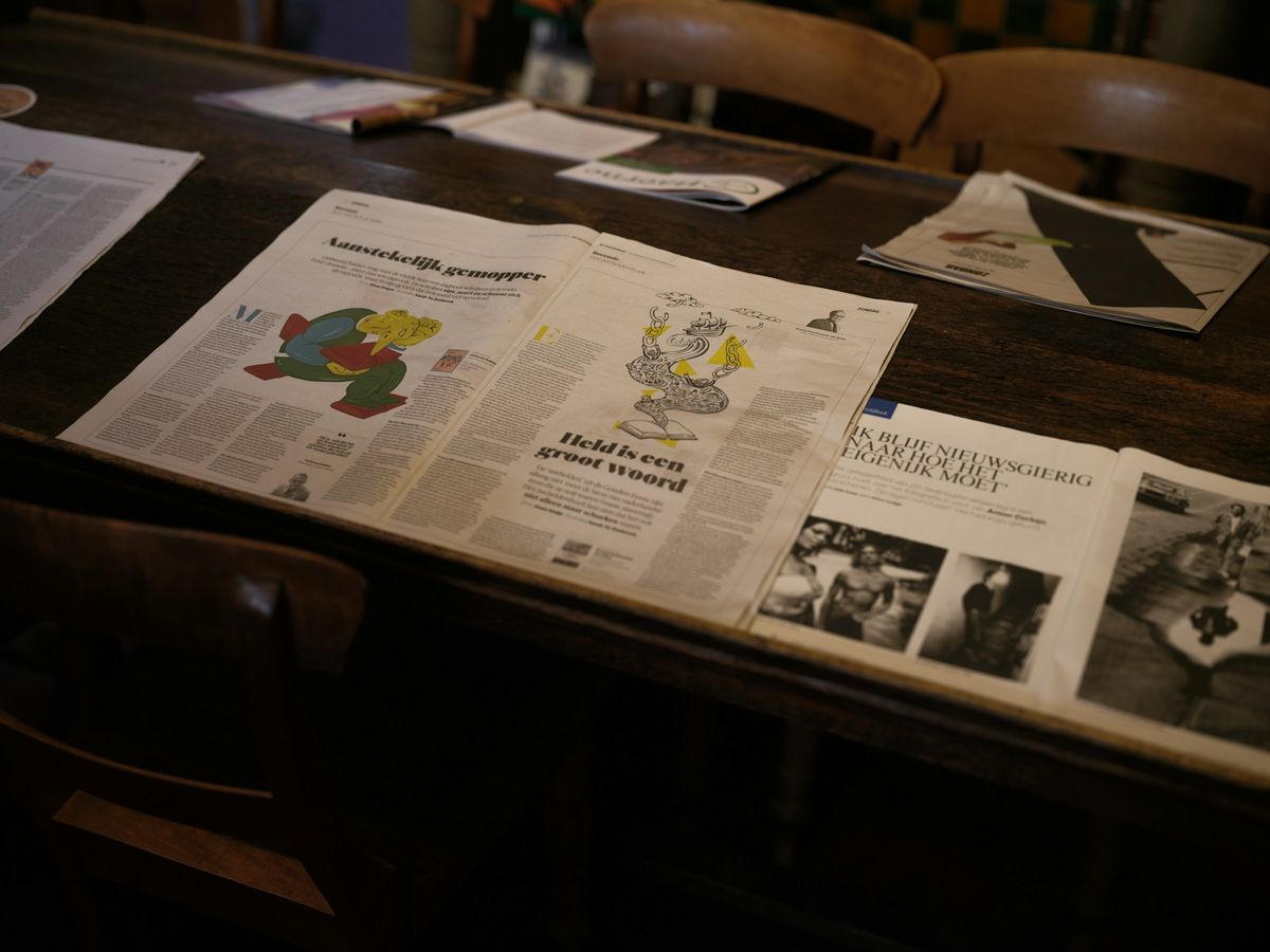 Newspaper features with large illustrations spread open across a dark wooden café table