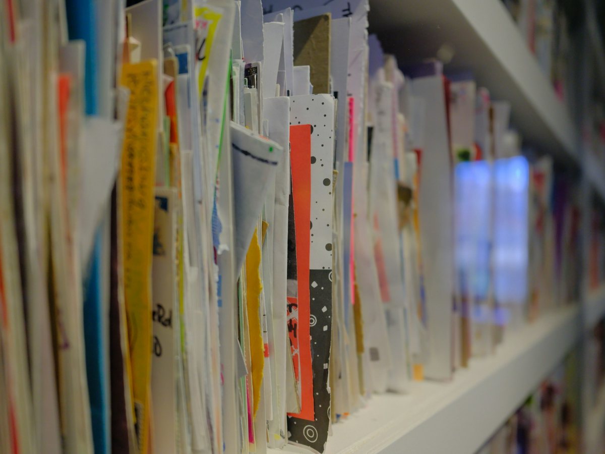 A dense row of colourful printed pieces standing upright on a white shelf