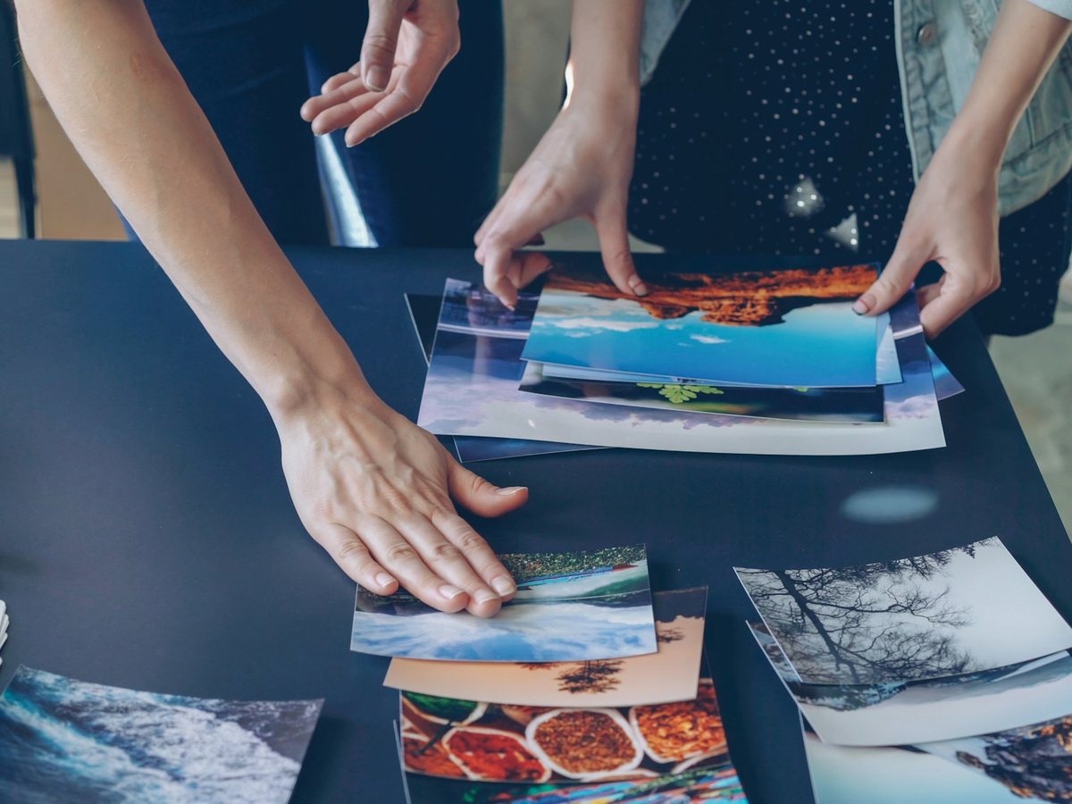 Hands arrange printed photographs and colour swatches across a dark table