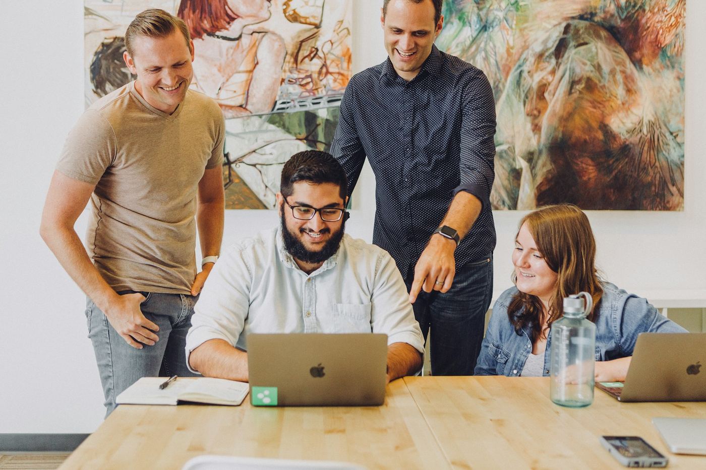 Four colleagues gathered around a laptop, smiling at something on the screen.