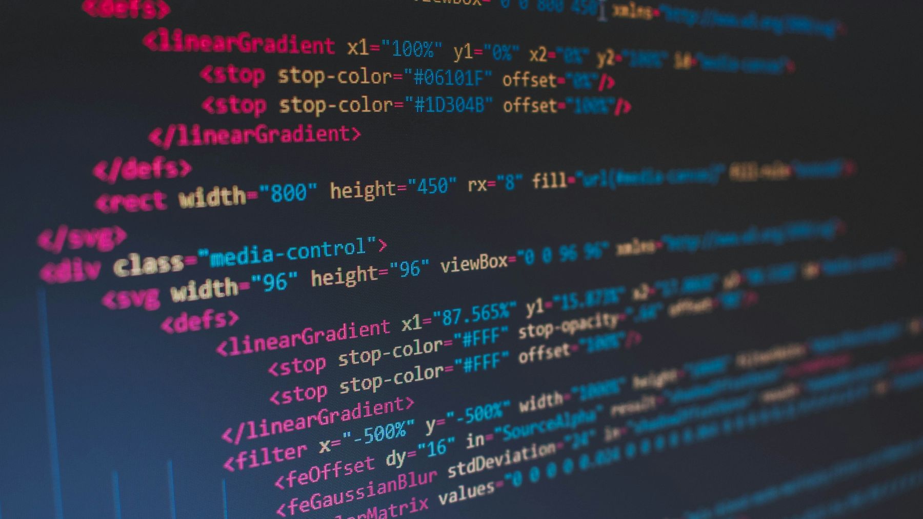 Code on a screen in close-up: SVG gradient and filter definitions in pink, blue and white on a dark editor.