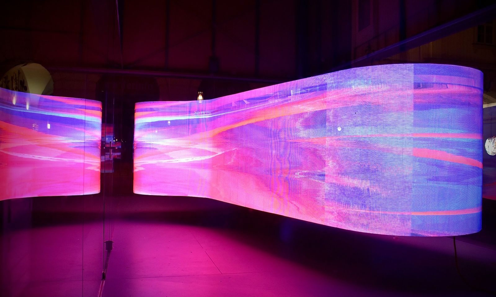 A curved LED screen glows with flowing pink and violet light in a dark room.