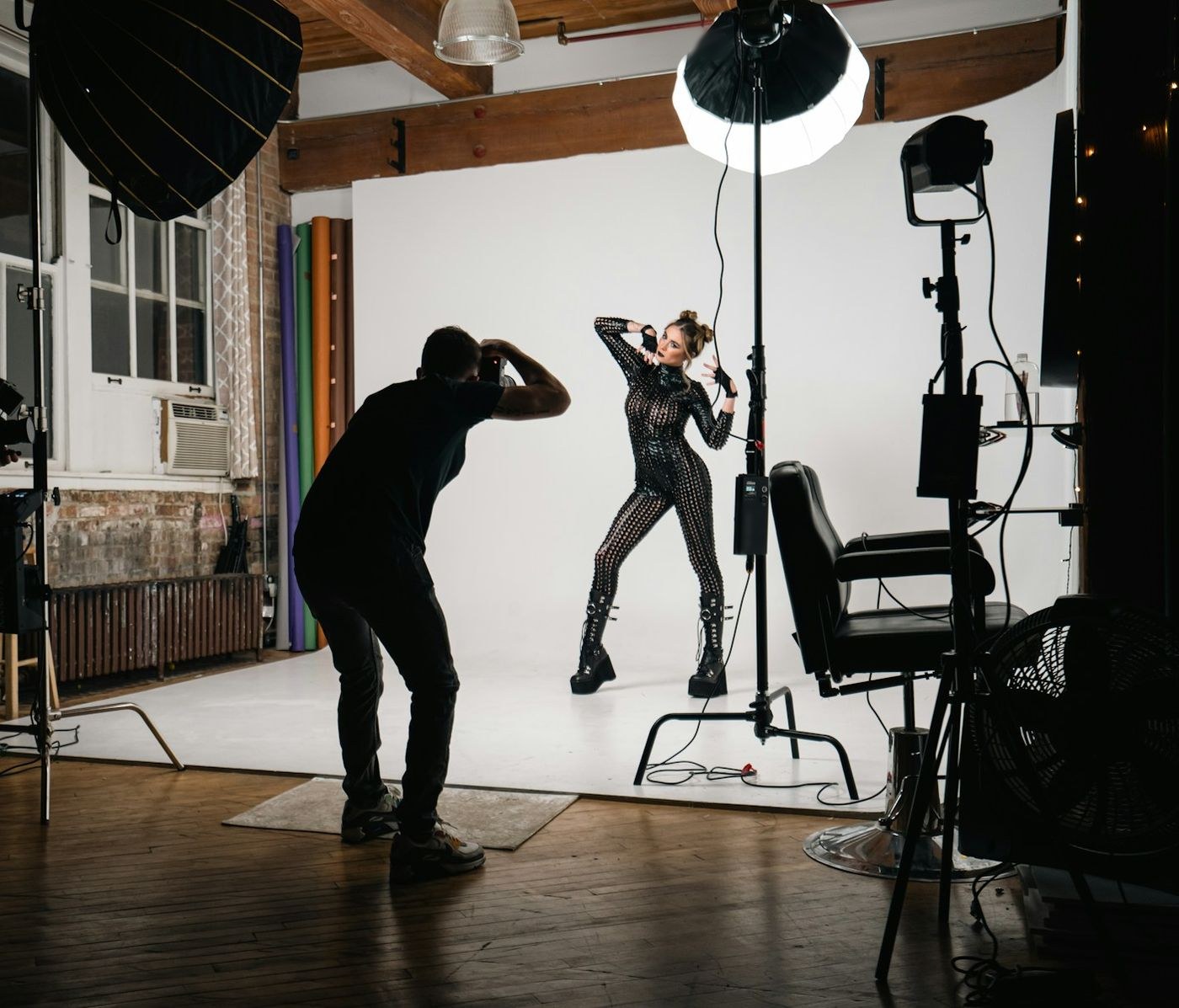 A photographer shoots a model against a white backdrop in a lit studio while a second camera films.