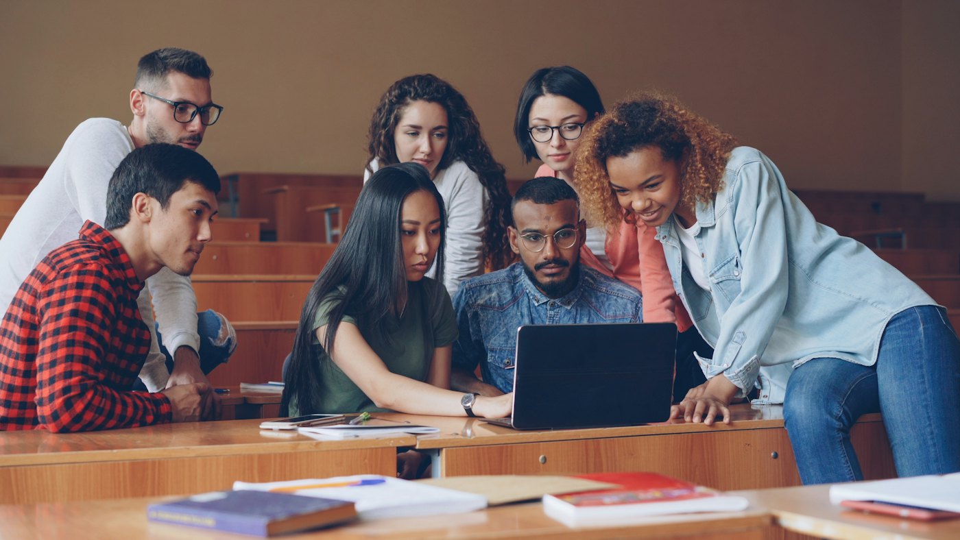 Students gather around a laptop in a lecture hall.