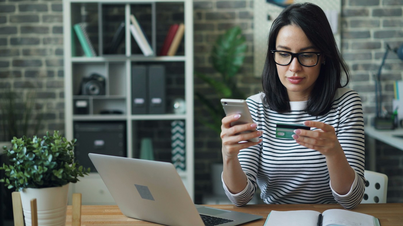 A woman pays on her phone while holding a bank card.