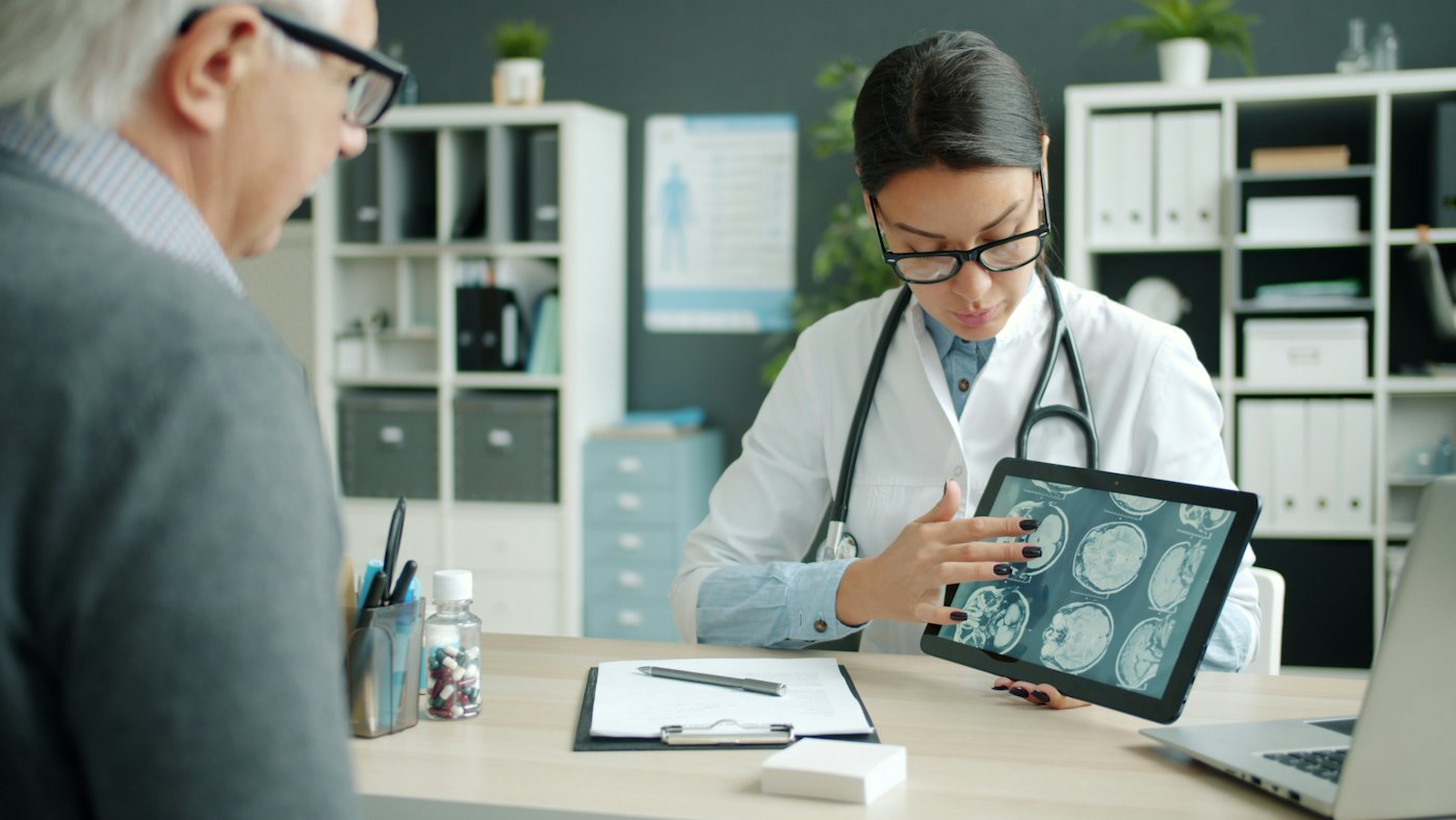 A doctor shows a patient a scan on a tablet.
