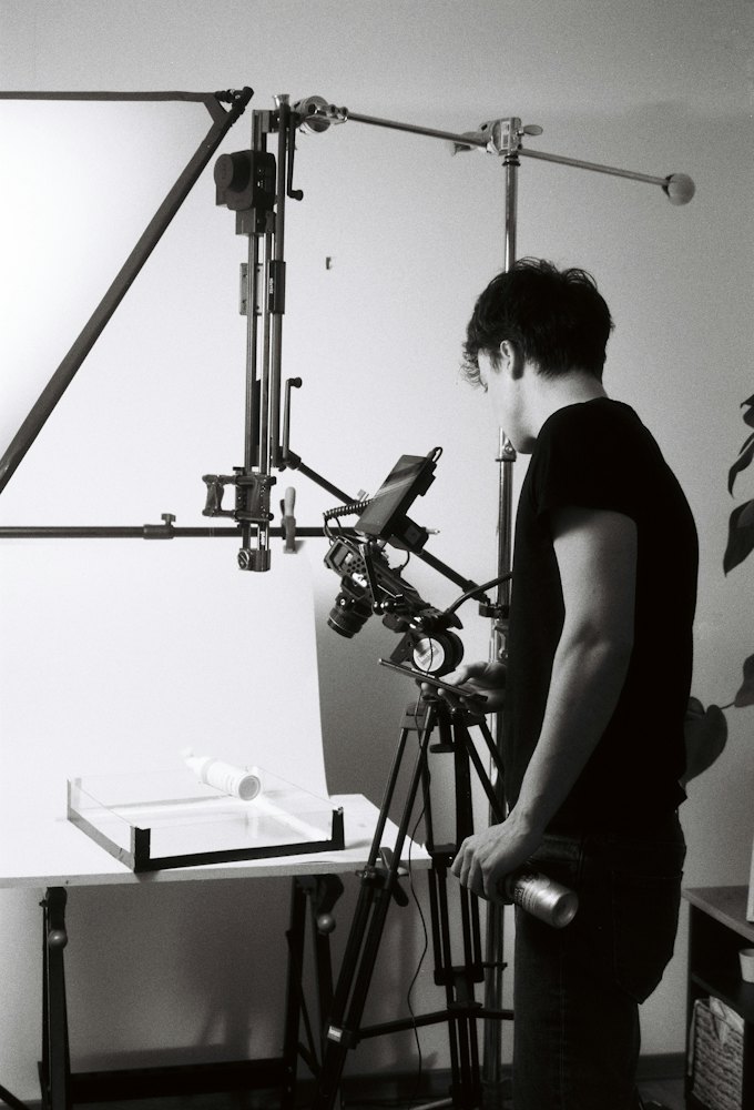 A photographer sets up a camera on a stand over a white tabletop set.