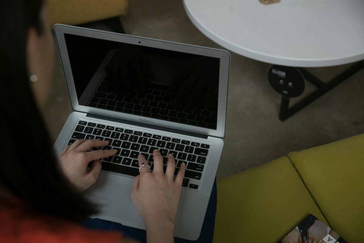 Seen from above, a person types on a laptop beside a small round table.