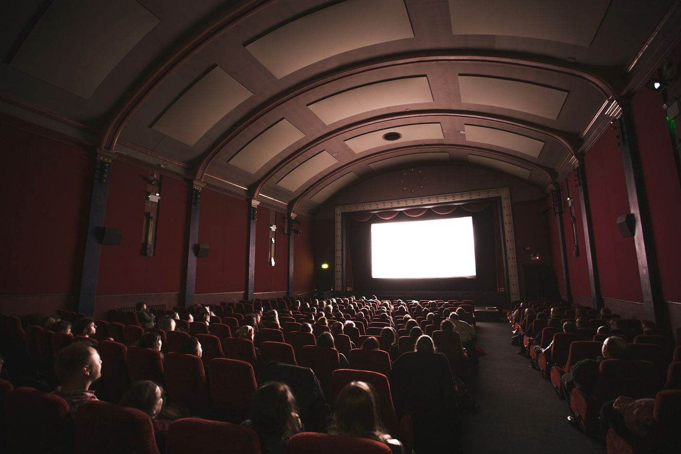 An audience watches a bright screen in a vaulted, red-walled cinema