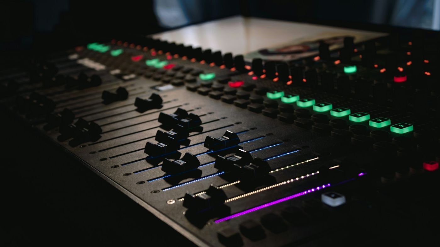 Close-up of faders and lit buttons on a mixing console in a dark room