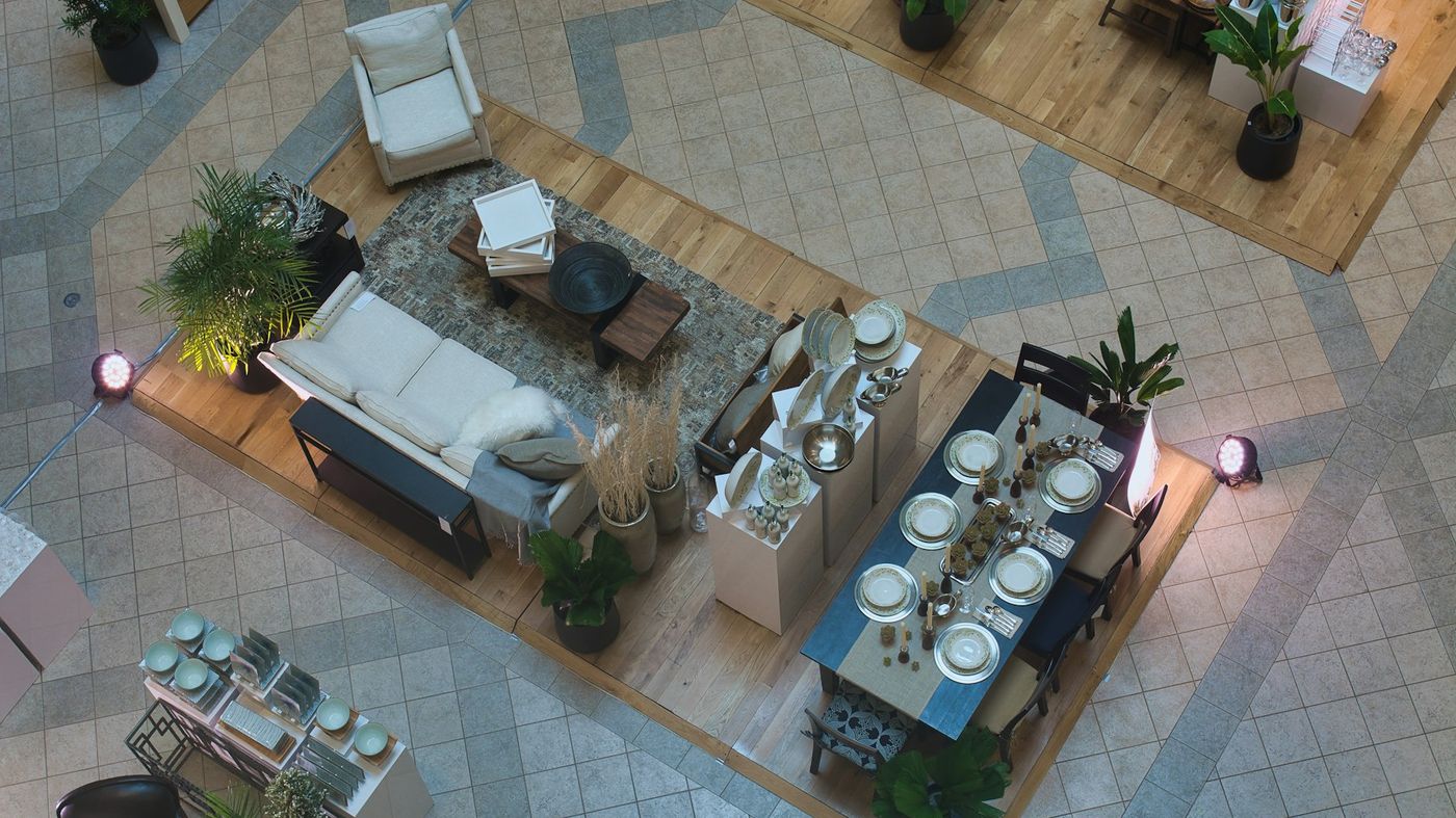 An overhead view of furniture staged as room sets on a showroom floor: a sofa, a dining table and tableware