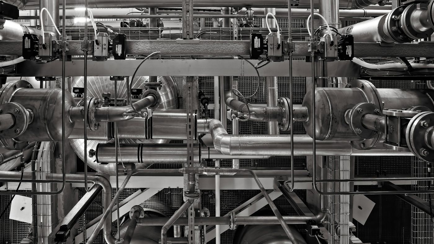 A dense network of steel pipes, valves and instruments in a plant, in black and white