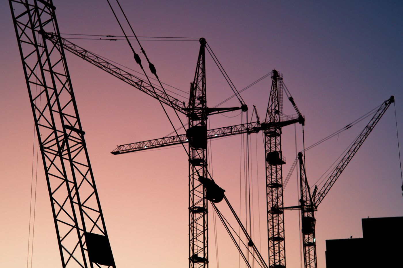 Silhouettes of tower cranes against a pink evening sky
