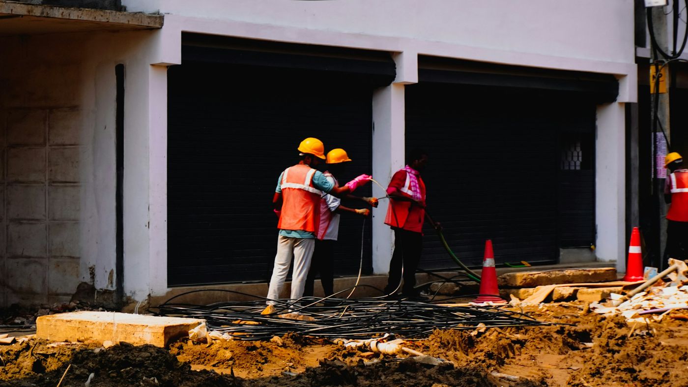 Workers in hard hats and high-visibility vests handle cables at a construction site