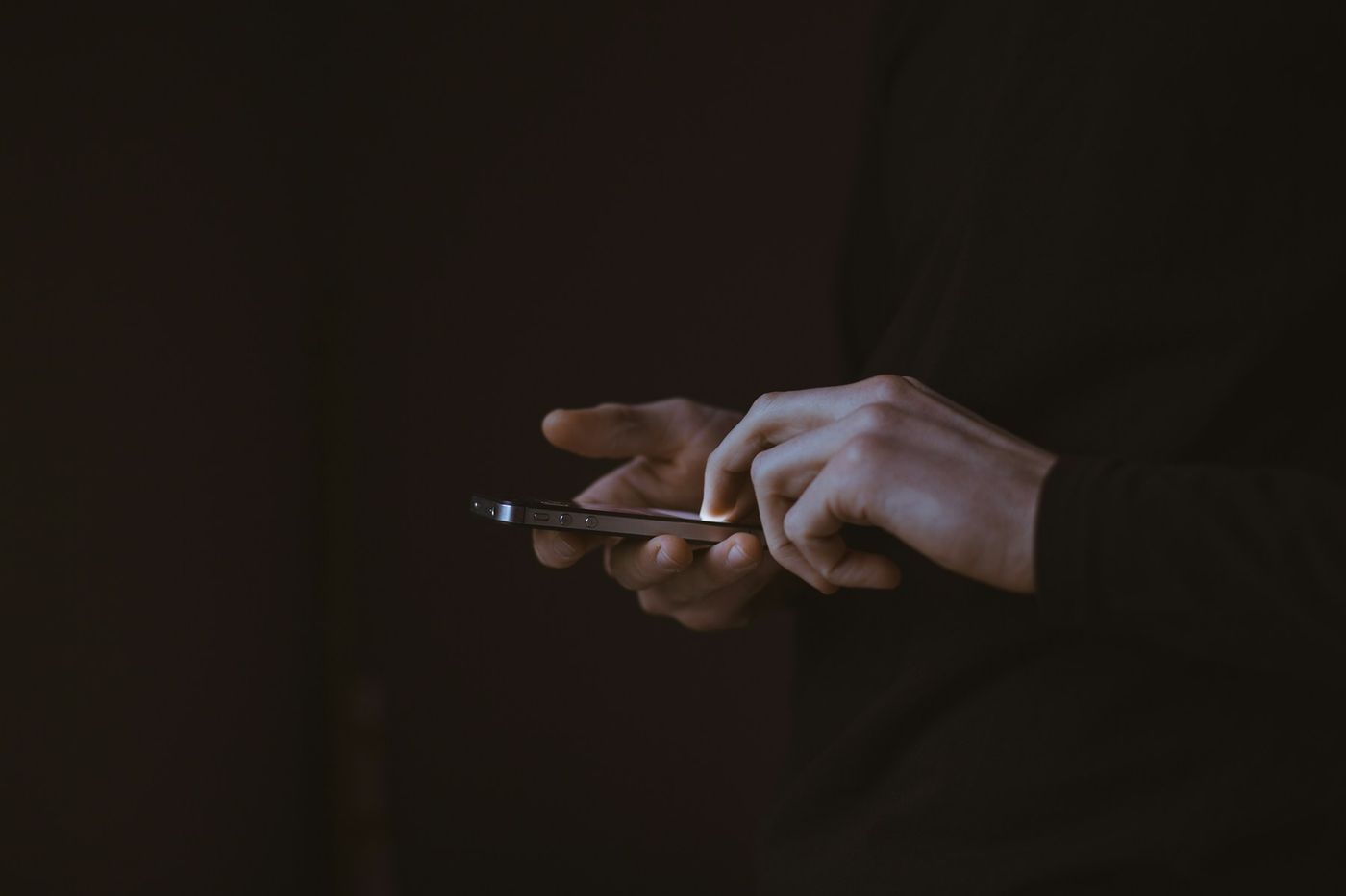 Two hands hold and tap a phone against a dark background