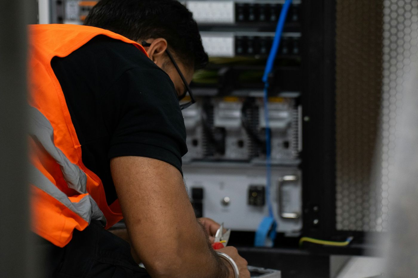 A technician in a high-visibility vest works on equipment at an open server rack