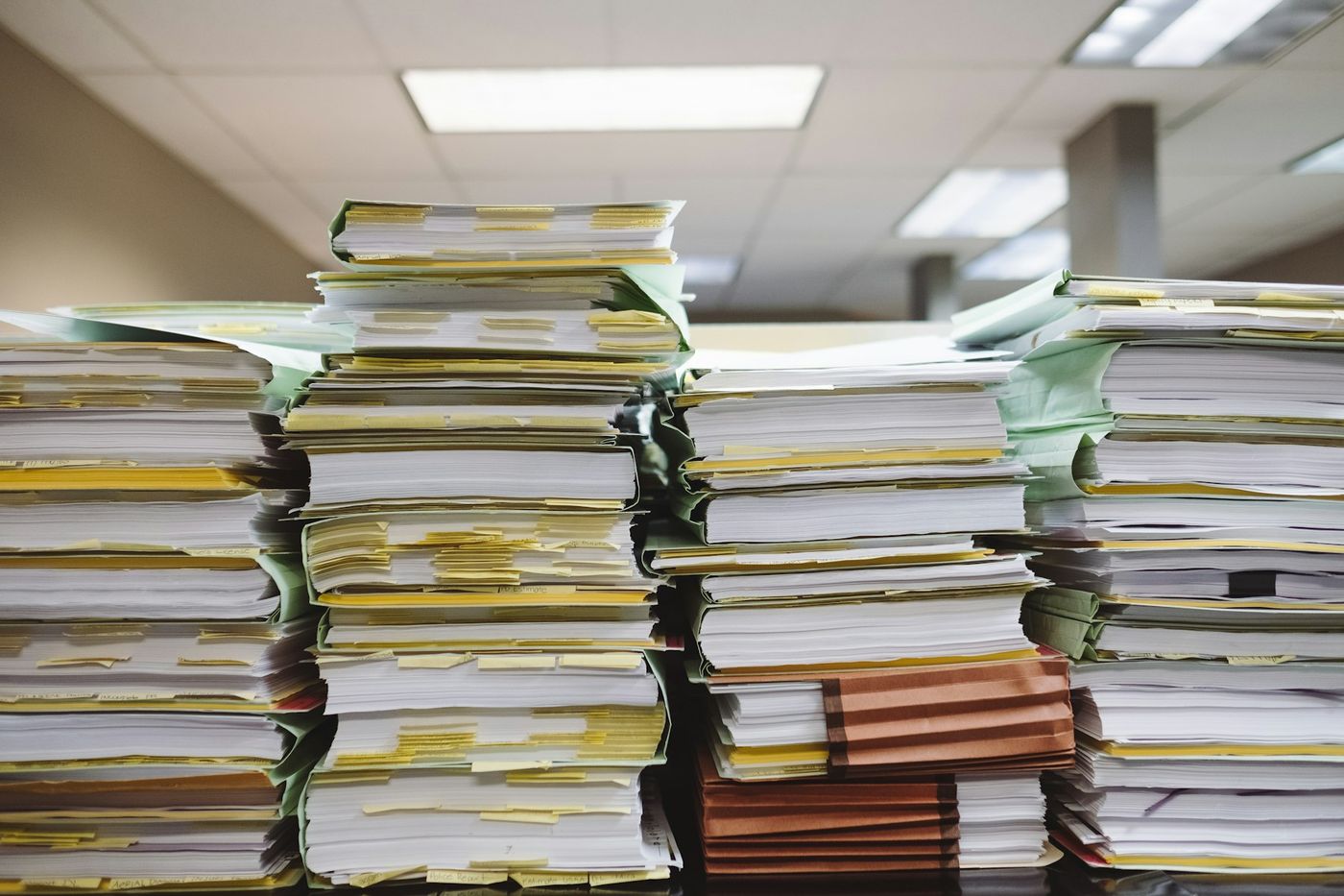 Tall stacks of paper files with yellow tabs on an office table