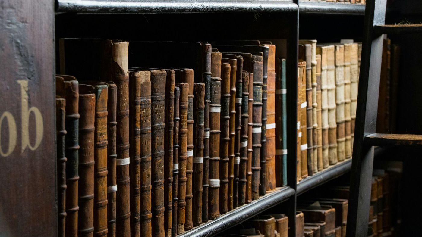 Rows of old leather-bound books on dark wooden library shelves