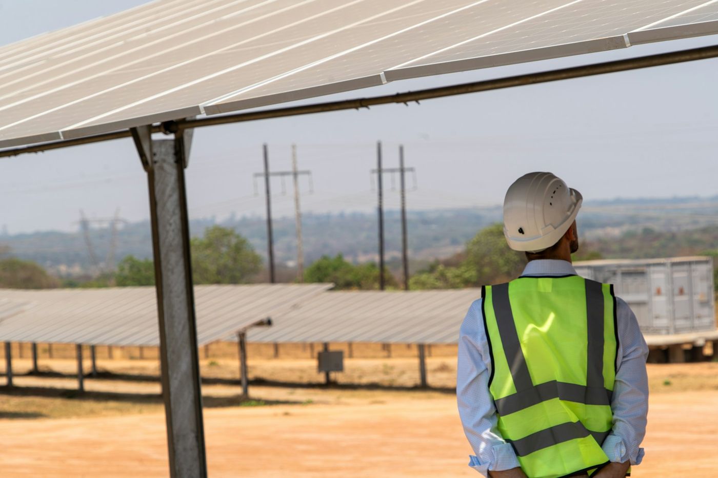An engineer in a hard hat and high-visibility vest looks across rows of solar panels