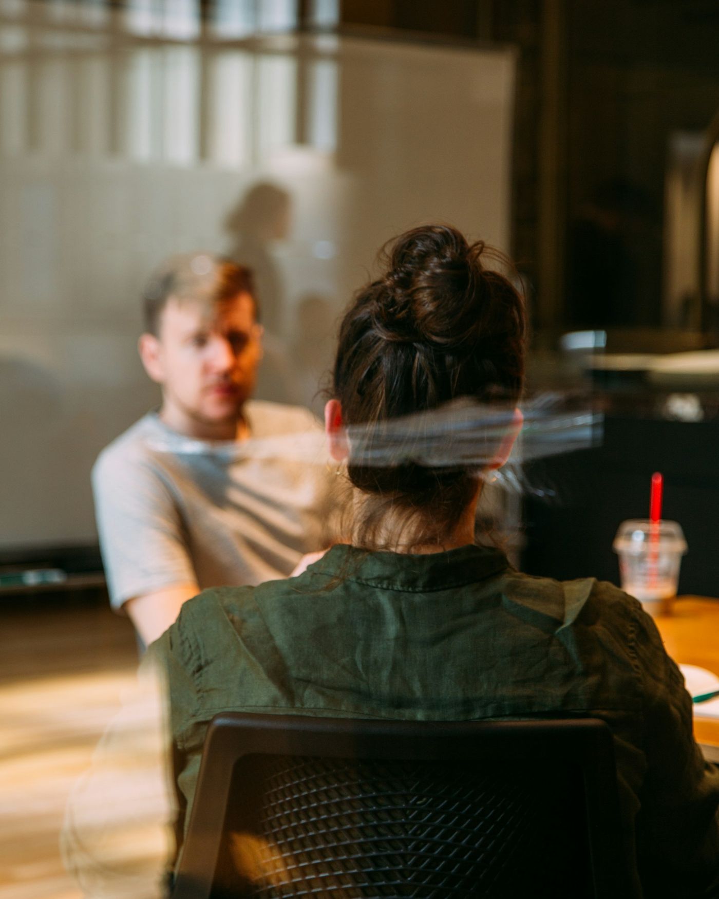 A candidate faces an interviewer across a table, seen through a glass partition