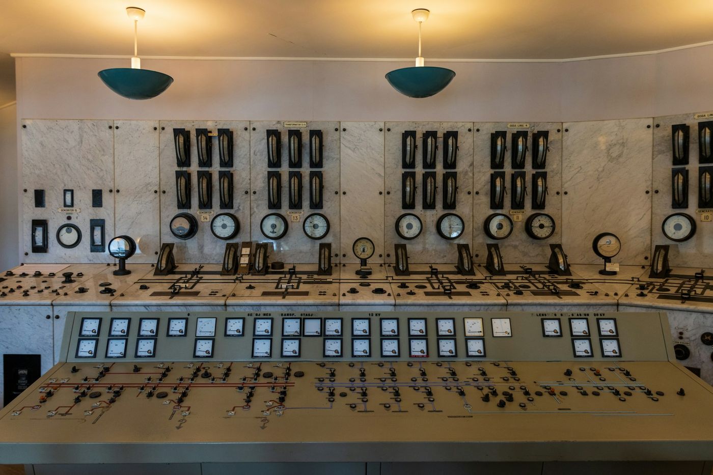 A control room with rows of dials, switches and gauges on a long console