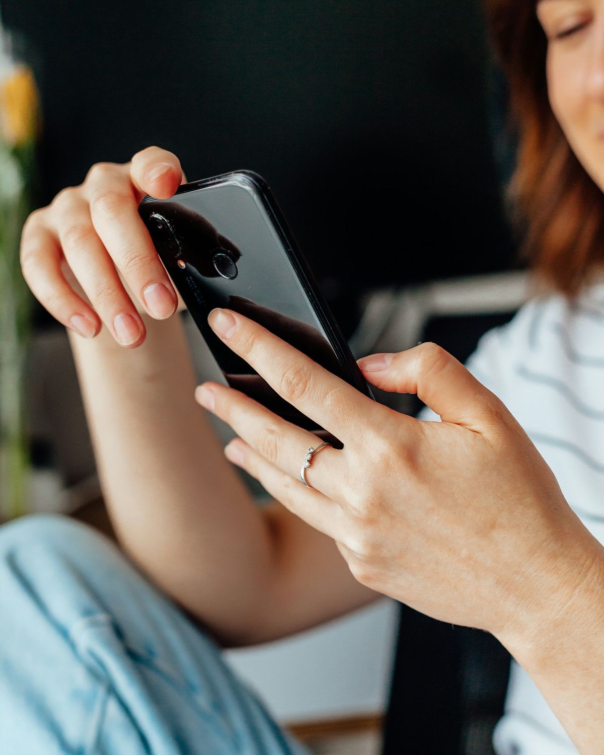 A woman in a striped top reads on a smartphone held in both hands