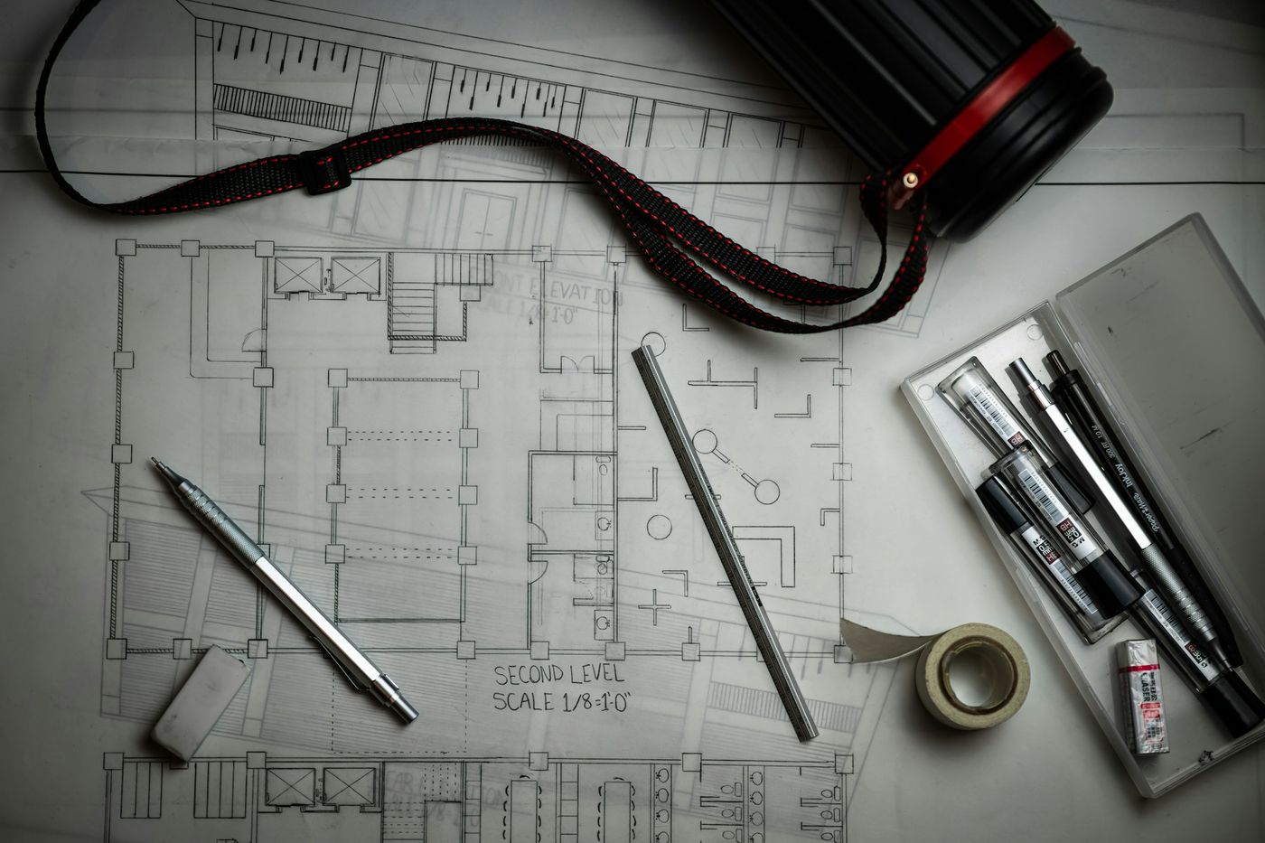 Architectural floor plans with a pencil, pens and drafting tools on a desk