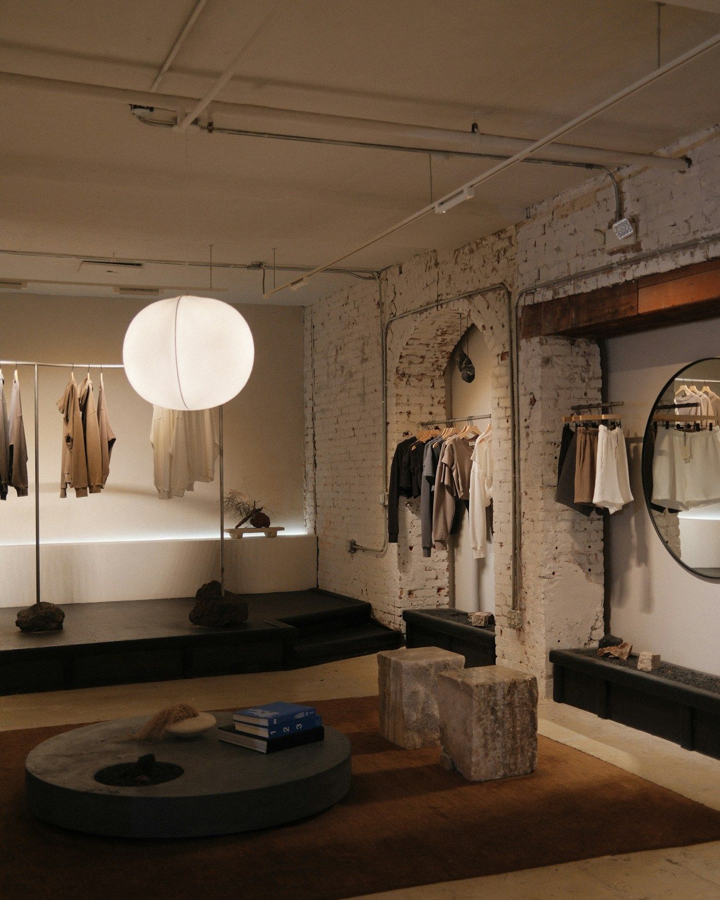 A calm boutique interior with clothing rails, a paper lantern and low display plinths