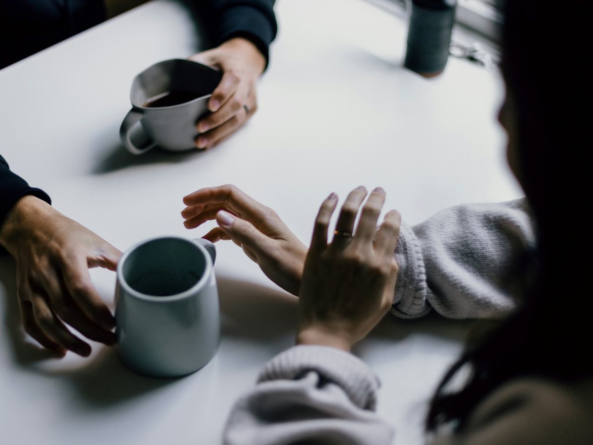 Hands and coffee mugs across a white table in the middle of a conversation