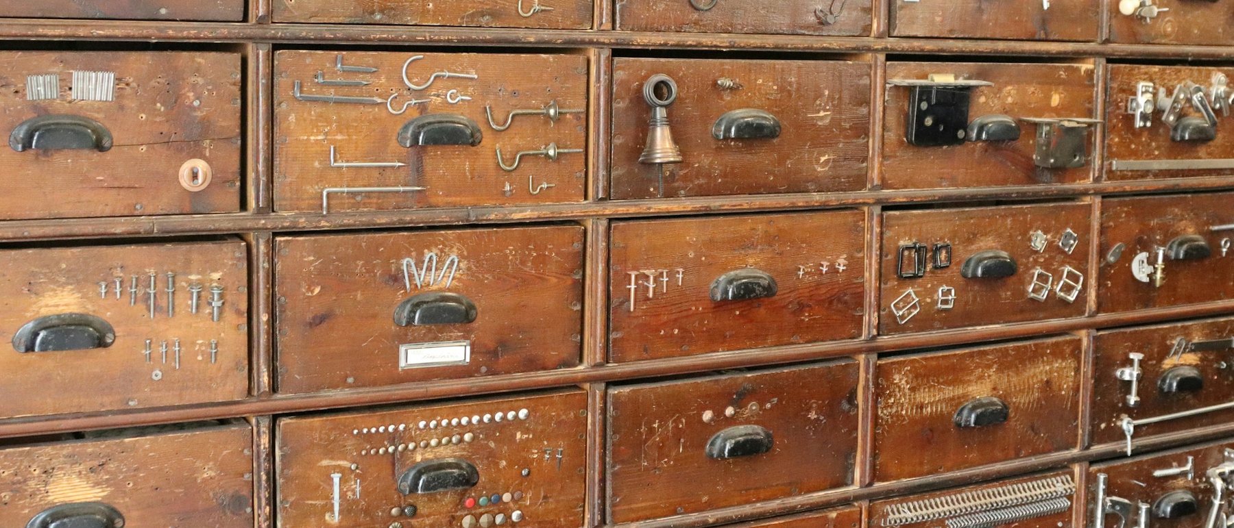 A wall of old wooden drawers, each showing the hooks, hinges or catches it holds on its front