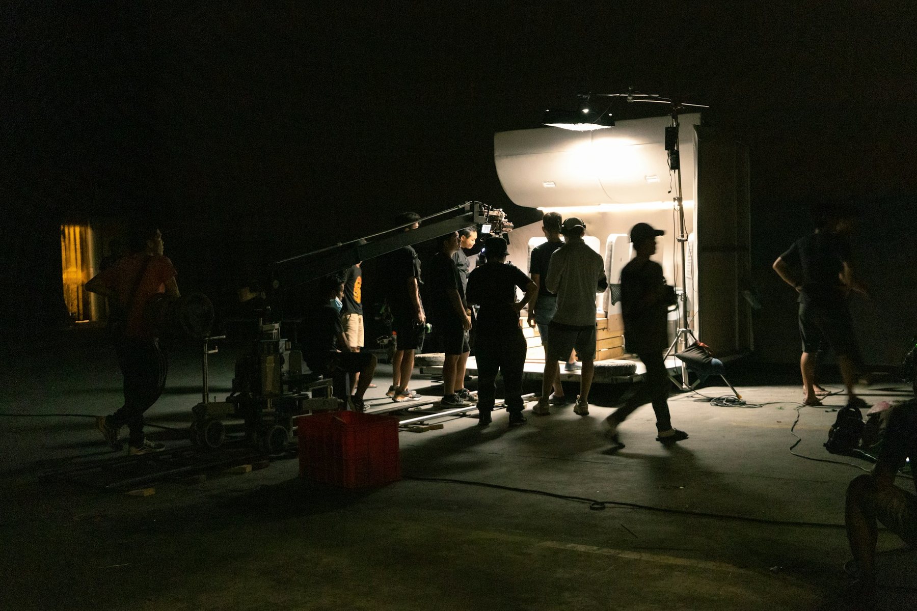 A crew at night around a lit set built inside a container, a camera on a crane arm
