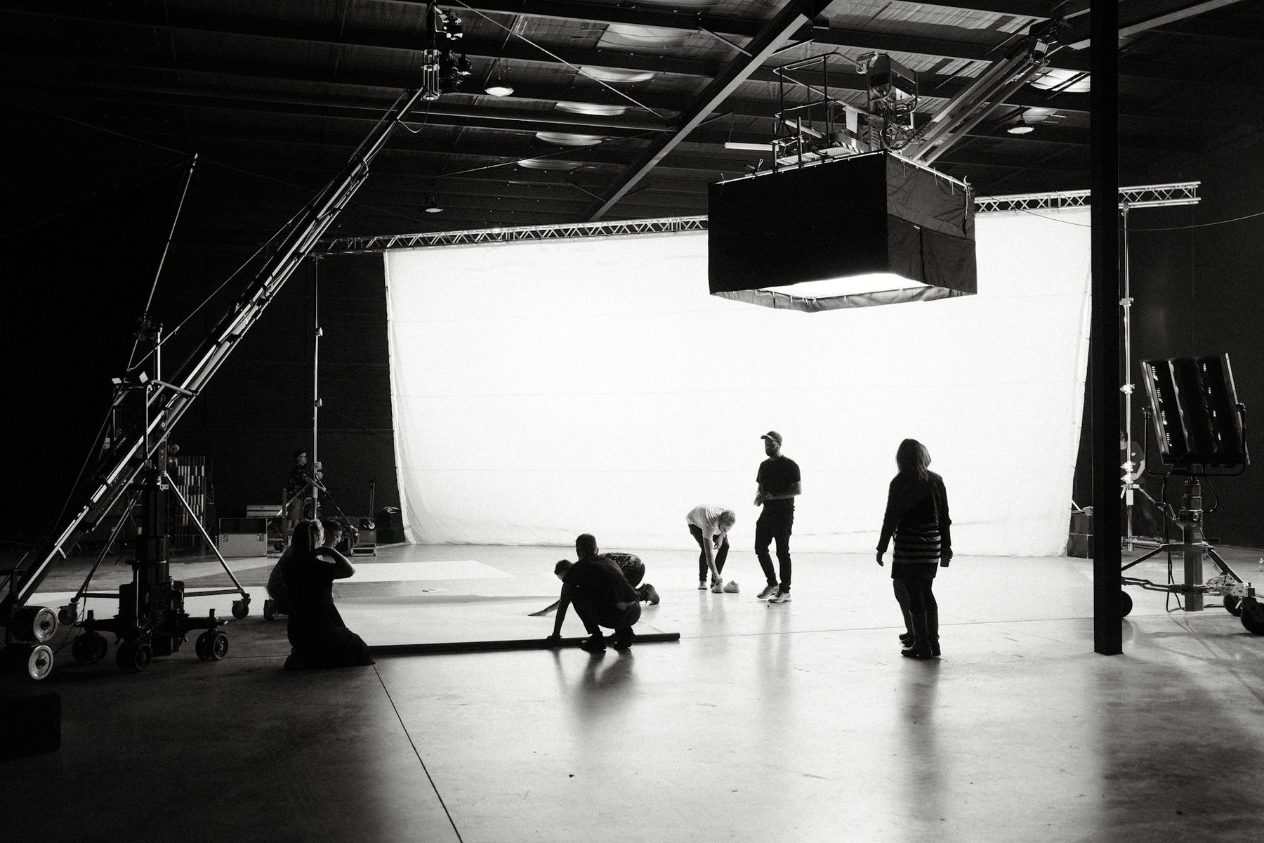 A crew preparing a white cyclorama stage under a large overhead soft light